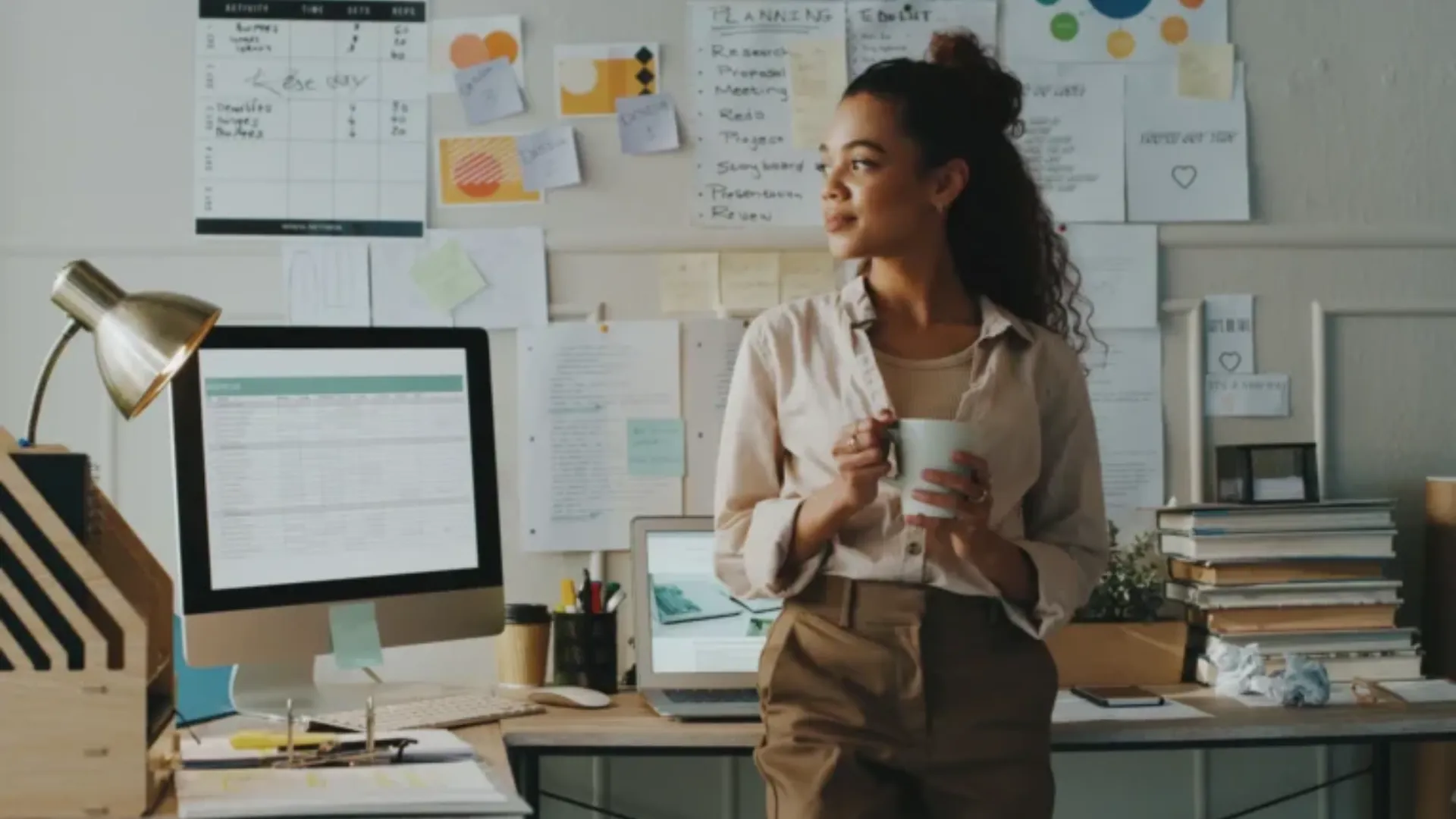 A woman holding a cup, standing in a creative workspace.