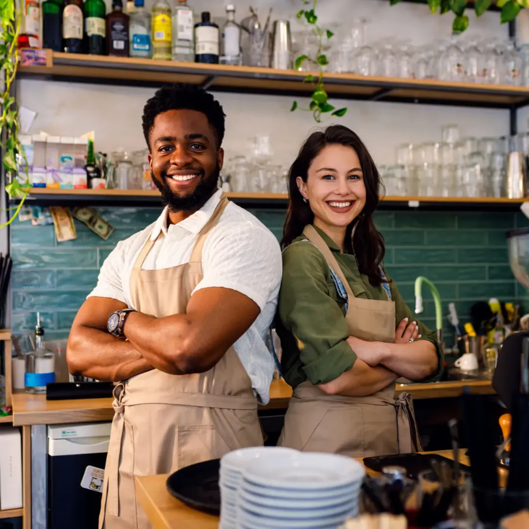 Two cheerful baristas posing confidently behind the coffee bar.