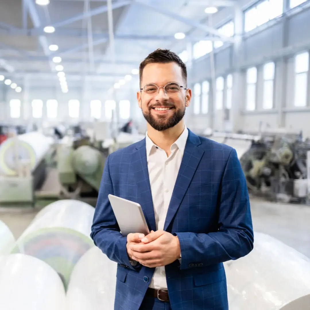 Smiling businessman in a factory holding a tablet.